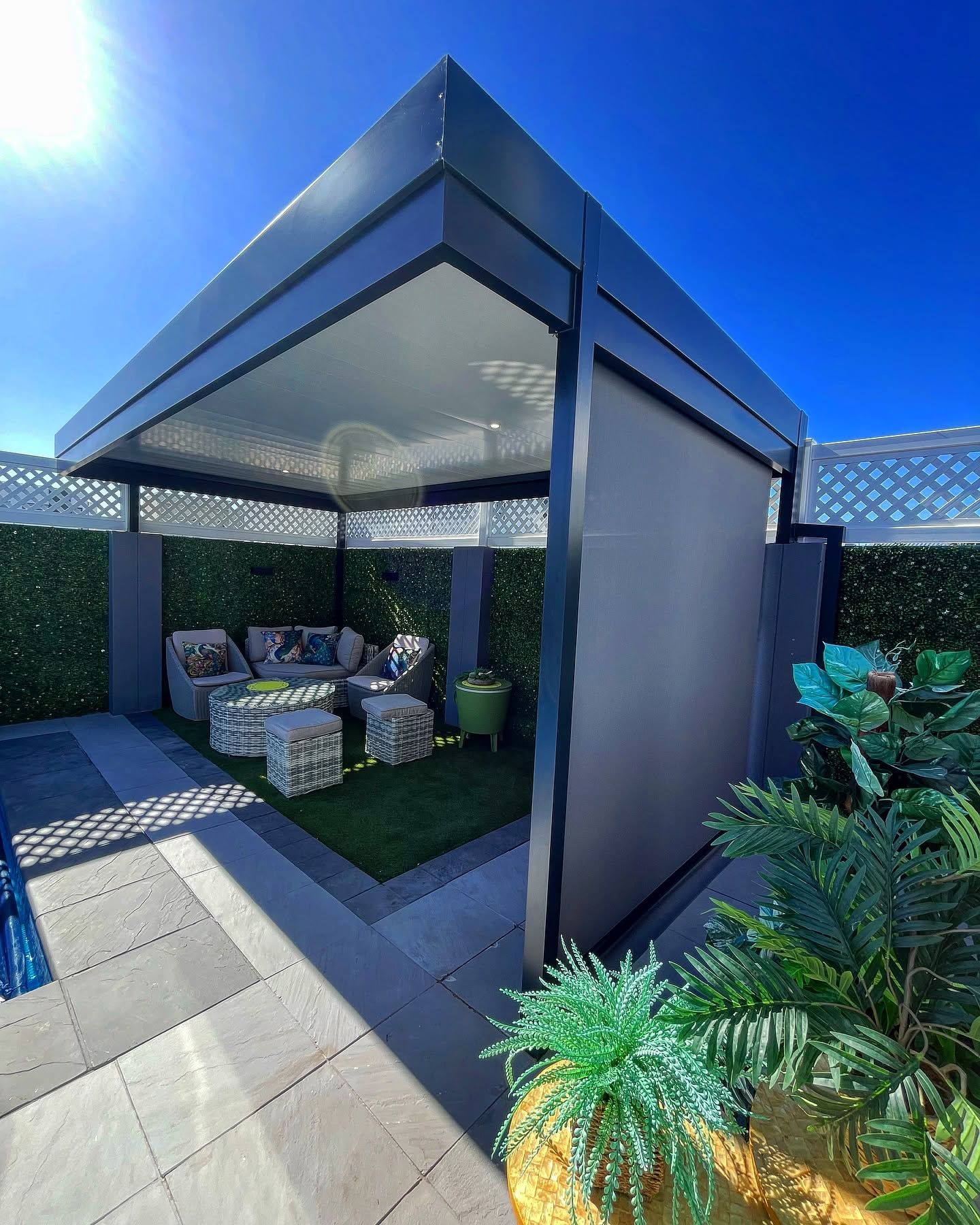 Free-standing charcoal louvre awning over an outdoor lounge with a drop-down side screen