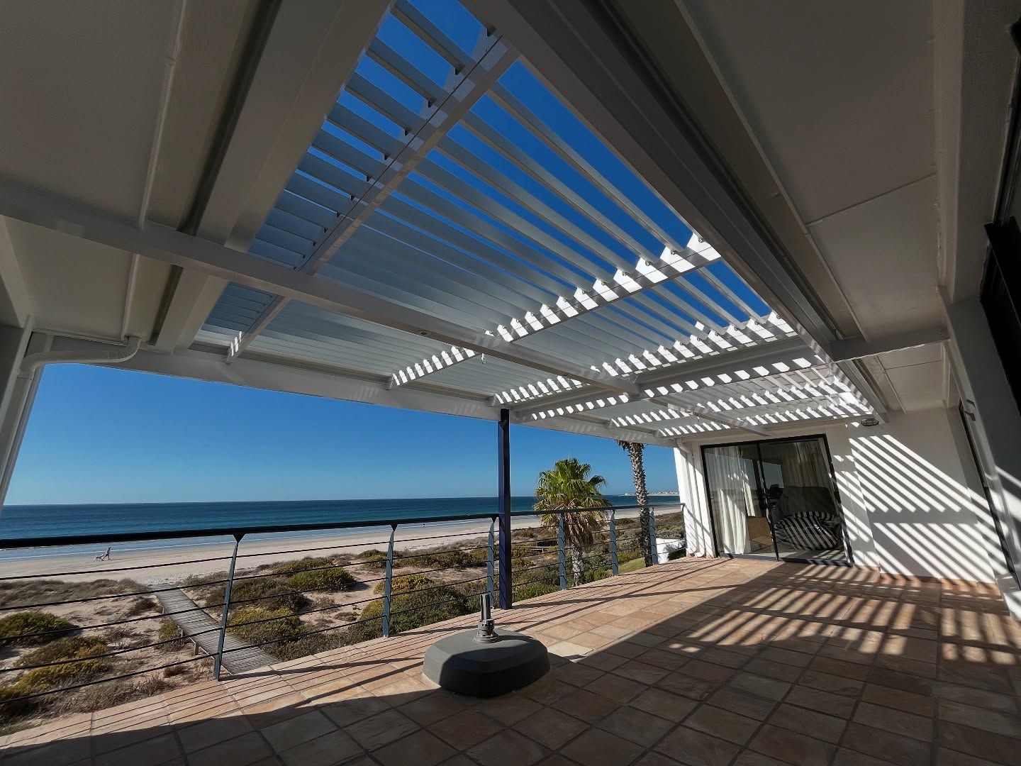 White louvre awning over a beachfront patio, louvres open to the sky